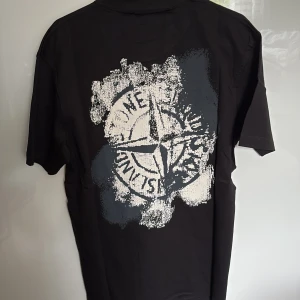 Svart t-shirt från Stone Island - Säljer en svart t-shirt från Stone Island med stort tryck på ryggen och logga framtill. T-shirten har rund hals och korta ärmar. Storlek S - nytt skick är inte använd. (Lappar kvar) passar 170-180 