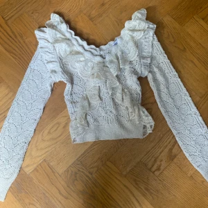 Vit spetsblus med volang från Zara - Superfin vit blus från Zara i spets med volangdetaljer och lång ärm. Blusen har en v-ringad halsringning och är perfekt för dig som gillar romantisk stil. Säljer då den inte kommer till användning längre.
