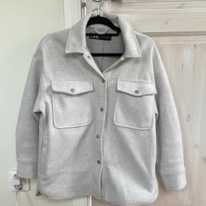  Zara overshirt  - Säljer en ljusgrå overshirt från Zara med stora bröstfickor och knappar framtill. Jackan har klassisk krage och lång ärm, perfekt för lager-på-lager-stil. Materialet känns mjukt och har en ull-liknande känsla. Helt ny och använt den en gång