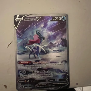 Pokémonkort Suicune V - Säljer ett holografiskt Pokémonkort av Suicune V med 210 HP. Kortet har en glittrig yta och visar Suicune i ett snöigt landskap. Det har attackerna Fleet-Footed och Blizzard Rondo. Perfekt för samlare eller Pokémonfans!