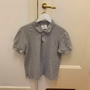 Grå och svart pikétröja från The Shirt Factory - Två klassiska pikétröjor från The Shirt Factory, en i grått och en i svart. Båda har krage, knappslå och korta ärmar. Perfekta för en clean och enkel stil. Bra passform, lite kortare modell.  99kr styck, 150kr för båda! 