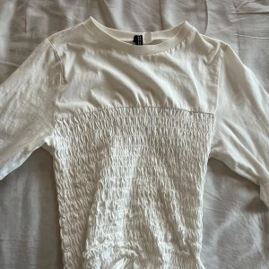 Vit kortärmad topp från H&M Divided - Säljer en vit kortärmad topp från H&M Divided i storlek XXS. Toppen har smockad midja och bröstparti vilket ger en snygg och bekväm passform. Perfekt till jeans eller kjol för en stilren look. 