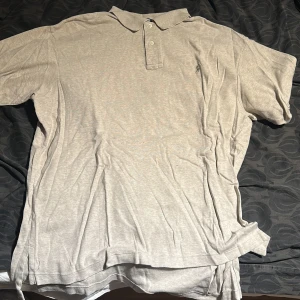 Beige pikétröja från Polo Ralph Lauren - Klassisk beige pikétröja från Polo Ralph Lauren med krage och två knappar framtill. Liten broderad logga på bröstet. Perfekt för en avslappnad och stilren look.
