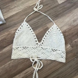 Vit virkad croppad linnetopp - Säljer en handvirkad vit croppad linnetopp med knytband i nacken och ryggen. Toppen har ett vackert spetsmönster och är perfekt för sommaren. Passar till festival eller strandhäng! Aldrig använd 