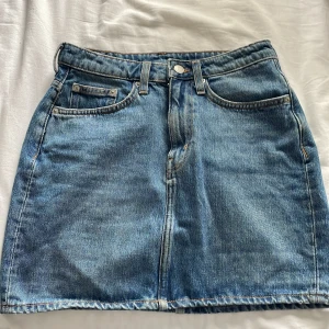 Jeanskjol från Weekday - Säljer en klassisk blå jeanskjol från Weekday i modell 'Wend skirt marfa blue'. Kjolen har fem fickor, knapp- och dragkedjestängning samt bälteshällor. Perfekt basplagg med normal passform och kort längd.