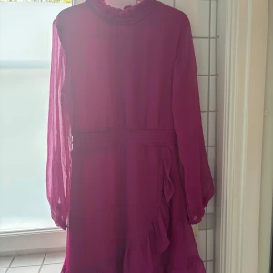 Mörkrosa chiffongklänning med volang  - Säljer en mörkrosa chiffongklänning med volang. Klänningen har fina detaljer runt hals, knäppning i nacke och markerad midja. Ärmarna i lätt transparent chiffongtyg. En favorit som min dotter nu vuxit ur nu, i fortsatt jättefint skick. Perfekt till sommarens kalas och fester. 299kr