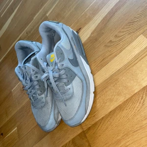 Grå Nike Air Max sneakers😮‍💨 - Säljer ett par grå Nike Air Max sneakers med gula detaljer på loggan. Skorna har snörning, rund tå och en synlig luftbubbla i sulan. Perfekta för dig som gillar klassisk streetstil och vill ha bekväma sneakers till vardags.