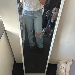 Ljusblå jeans med hål på knäna - Säljer ett par ljusblå jeans med raka ben och slitna hål på båda knäna. Jeansen har klassisk femficksdesign och normal passform. Perfekta för en avslappnad och trendig look. Storlek 32 längd 34