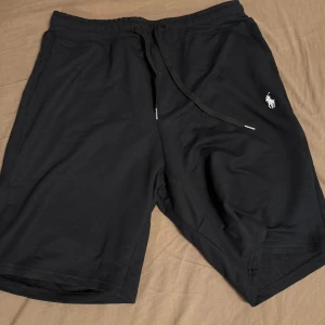 Svarta shorts från Polo Ralph Lauren - Svarta shorts med dragsko i midjan och två sidofickor. Klassisk Polo Ralph Lauren-logga broderad i vitt på vänster ben. Mjukt material och avslappnad passform, perfekta för sommaren.