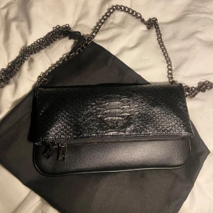 Svart zadigväska med ormskinnsmönster - Svart zadig väska med ormskinnsmönster. Kommer ej till användning mer. Den har inga defekter alls syns knappt att den är använd. Dustbag medkommer samt en längre kedja som jag tagit av💝