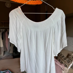 Vit offshoulder blus från Bik Bok - Säljer en vit offshoulder blus från Bik Bok i storlek 34. Toppen har en lös passform med bred resår upptill och korta ärmar. Luftigt lätt material. 