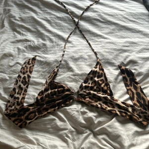 Går att pruta. Leopardmönstrad bikiniöverdel/topp med knyt - Säljer en snygg bikiniöverdel/topp med leopardmönster och knyt i nacken och ryggen. Triangelformade kupor och ringdetalj framtill. Perfekt för sommaren och strandhäng!