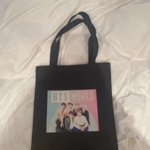 Svart tygkasse med BTS World-tryck - Säljer en svart tygkasse med långt axelband och ett stort färgglatt BTS World-tryck på framsidan. Perfekt för dig som älskar K-pop och vill bära med dig dina saker med stil. Enkel och rymlig design. Det ända med väskan är att dragkedjanr trasig men har använt den utan den och det funkar lika bra. Plus så kan man su om den man har inte haft tid att göra det💕 Köptes från Wish för länge sedan. 