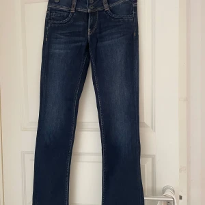 Mörkblå jeans från Pepe Jeans - Snygga mörkblå jeans från Pepe Jeans med raka ben och klassiska kontrastsömmar. Byxorna har normal midja och raka ben, samt bakfickor med dekorativ söm. Perfekta till vardags för en stilren look.