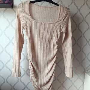 Beige ribbad långärmad klänning  - Säljer en beige ribbad klänning med lång ärm och fyrkantig ringning. Klänningen har en kroppsnära passform och är tillverkad i ett mjukt, stretchigt material. Finns tyvärr ingen lapp kvar, men skulle säga storlek s/m. Har ett litet hål men är ingenting som syns när man har på sig den 