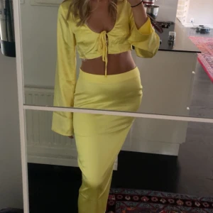 Gul satin set från NA-KD x Josephine HJ - Säljer ett gult satin set från NA-KD x Josephine HJ, topp långa ärmar och knyt framtill och midi kjol med dragkejda . Blusen har djup v-ringning och är tillverkad i ett glansigt, satinliknande material. Perfekt för midsommar, utekväll eller bara klä upp sig i sommarens färg! Storlek 36 i toppen och 38 i midikjolen!