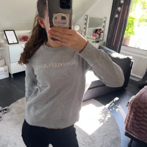 Grå sweatshirt från Calvin Klein Jeans - Säljer en ljusgrå sweatshirt från Calvin Klein Jeans med vit logga framtill. Tröjan har rund halsringning och långa ärmar. Perfekt basic att ha i garderoben!