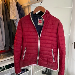 Röd pufferjacka från Colmar - Fet röd colmarjacka som är lagom för våren. En del av dunet i jackan har försvunnit vilket gör att den är lite tunnare. Den är väl använd o har lite fläckar och slitningar, se bilder. En dragkedja på fickan har också ramlat av. Den har den mycket kvar att ge och de är inget som syns när man använder den. Hör av er vid frågor!