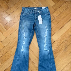 Blå bootcut jeans med slitningar - Snygga ljusblå jeans med bootcut passform och slitna detaljer längs benen. Klassisk femficksmodell med normal midja och dragkedja. Perfekta för en avslappnad och trendig look. Helt nytt skick💕