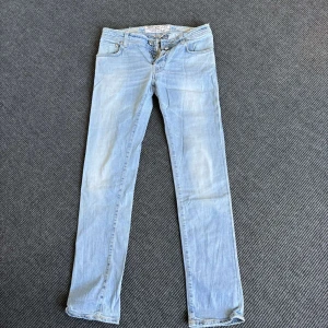 Ljusblå jeansbyxor från Jacob Cohen - Säljer ett par ljusblå jeansbyxor från Jacob Cohen med klassisk femficksdesign och knäppning med knappar. Jeansen har raka ben och är tillverkade i mjukt denimtyg. Perfekta för en avslappnad stil.