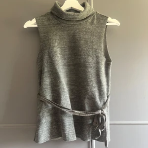 Knyt topp från Zara  - Säljer en grå/grön aktig knyt topp ifrån Zara. Toppen har en hög polokrage och ett band i midjan som knyts i sidan för en snygg detalj. Perfekt att styla med jeans eller kjol. Hör av dig vid frågor💗