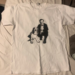 Vit t-shirt med tryck av Ulf Kristersson  - Säljer en vit t-shirt med ett svart tryck av Ulf Kristersson och hans hundT-shirten har en klassisk passform och korta ärmar. Perfekt för en avslappnad stil.
