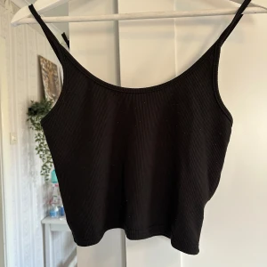 Svart ribbad linnetopp från SHEIN - Säljer en svart ribbad linnetopp från SHEIN med smala axelband. Perfekt för sommaren och enkel att matcha med olika outfits. Toppens material är mjukt och stretchigt för en bekväm passform.