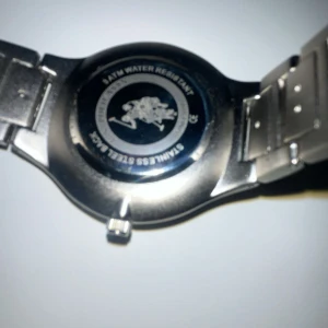 Silverfärgad klocka från U.S. Polo Assn. - Stilren herrklocka från U.S. Polo Assn. med svart urtavla och silverfärgat armband i rostfritt stål. Klockan har tydliga indexmarkeringar och logotyp med polospelare på urtavlan. Levereras i original ask.