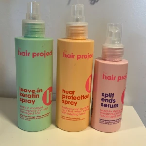 The Hair Project stylingprodukter - Tre olika hårsprayer från The Hair Project: leave-in keratin spray i mintgrön flaska, heat protection spray i gul flaska och split ends serum i ljusrosa flaska. Alla med spraymunstycke och tydlig text på framsidan.