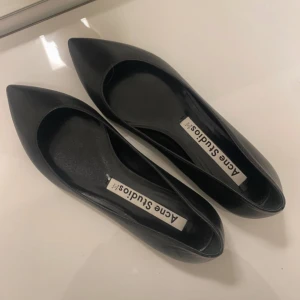 Svarta ballerinaskor från Acne Studios - Stilrena svarta ballerinaskor från Acne Studios med spetsig tå. Skorna är tillverkade i skinn och har en elegant och minimalistisk design. Perfekta för sommaren🩷 Passar även 38