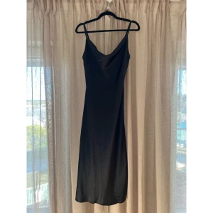 Svart långklänning i satin från Anna Dani - Säljer en svart långklänning från Anna Dani med smala axelband och en något draperad urringning. En elegant klänning som passar perfekt till bal eller annan finsittning! Köpt av mina föräldrar i Milano deras butik för €70. Tyvärr lite liten för mig så aldrig använd.