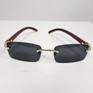 Svarta rektangulära solglasögon med gulddetaljer - Stilrena solglasögon med svarta rektangulära glas och tunna guldfärgade bågar. Skalmarna är bruna och har en elegant minimalistisk design. Perfekta för dig som vill ha en modern och trendig look.