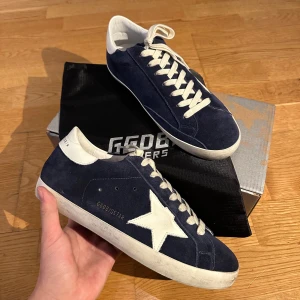 Golden Goose Mörkblå! - Säljer ett par mörkblå sneakers från Golden Goose med vit stjärndetalj på sidan, storlek 43 innersulan är 27.5cm. Dem är helt oanvända och det medkommer även dustbag och lådan vid köp! Helt oanvända till priset av bästa kvalite. Hojta till vid fler funderingar!