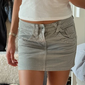 Ljusgrå jeanskjol med fickor - Säljer en ljusgrå jeanskjol med klassiska fickor fram och bak samt bälteshällor. Kjolen har en kort passform och stängs med dragkedja och knapp framtill. Perfekt för dig som gillar en enkel och stilren look.
