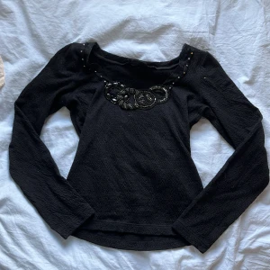 Svart långärmad topp med pärldetaljer - Säljer en skitsnygg svart långärmad topp med pärl- och paljettbroderi framtill vid halsen. Toppen har en lätt strukturerad yta och rund halsringning. Perfekt för dig som gillar unika detaljer och stilren design. Säljer pga att den inte kommer till användning! Skulle nog säga att den passar runt xs - s men är inte så säker, tyget är stretchigt så det passar flera storlekar. Kom privat för funderingar eller fler bilder💕