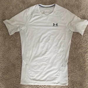 Under Armour Compression Shirt - Säljer en vit compression shirt då jag inte tycker om den längre, sitter jäkligt skönt och är i bra skick, namnlappen på nacken är dock lite sliten men annars är den bra, sitter som den ska och är snygg på! 😁