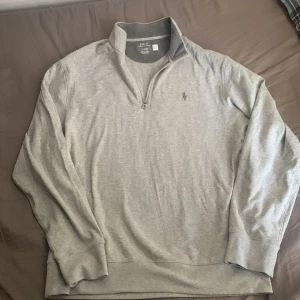 Grå långärmad tröja med dragkedja från Polo Ralph Lauren - Säljer en stilren grå långärmad tröja från Polo Ralph Lauren med halv dragkedja och broderad logga på bröstet. Perfekt för en avslappnad men snygg look. Mjuk bomullskvalitet och klassisk passform. Nypris 2000kr