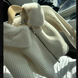 Vit stickad jacka med fuskpäls från Zara - Superfin vit stickad jacka från Zara med dragkedja och mjuk fuskpäls på kragen. Jackan är croppad och har långa ärmar, perfekt för att lyfta din outfit med en mysig touch. Jackan är sprillans ny och helt oanvänd, köpt för 700 kr!                                                              (PRIS KAN DISKUTERAS)