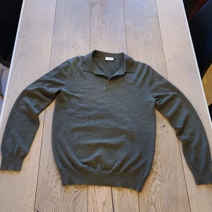 Grön merinoull pike ifrån John Henric - Snygg grön långärmad polotröja från John Henric i mjuk merinoull. Tröjan har klassisk krage och två knappar framtill. Perfekt för lager-på-lager och passar till många olika stilar.Den har ett litet hål som visas på bild 4 som lätt går att laga.