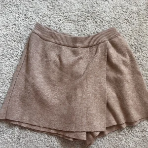 Beige stickad omlottkjol från Zara - Superfin beige stickad kjol från Zara med omlottdetalj framtill och bred resår i midjan. Kjolen har en mjuk och skön känsla, perfekt för en avslappnad men ändå snygg look.