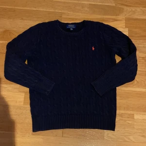 Mörkblå stickad tröja från Polo Ralph Lauren - Säljer en klassisk mörkblå stickad tröja från Polo Ralph Lauren med rund halsringning och kabelstickat mönster. Nypris är ca 1300kr. Den är i mycket bra skick fast den har används lite. Den passar mellan 155-170.