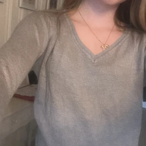 Grå långärmad stickad tröja - Mysig grå stickad tröja med v-ringning. Tröjan har lång ärm och en enkel, klassisk design som passar perfekt till vardags. Materialet känns mjukt och bekvämt mot huden.