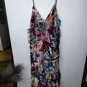 Blommig långklänning med smala axelband - Säljer en färgglad långklänning med blommigt mönster och smala axelband. Klänningen har en v-ringad front och är perfekt för varma dagar. Materialet känns lätt och luftigt, och färgerna går i rosa, blått, grönt och rött.