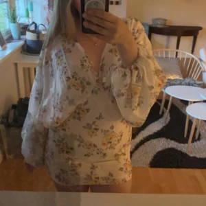 Blommig kortklänning med volang och v-ringning💓 - Superfin kortklänning i ljus färg med blommigt mönster. Klänningen är helt ny med prislapp, jag säljer den då jag tyckte den var lite för kort på mig. Klänningen är märkt som storlek 42, men den är lite liten i storleken och sitter mer som en 38. Hör av er om ni funderar över något!🤗🥰🥰☺️