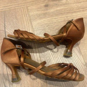 Brown dance shoes with heels and straps - Selling a pair of brown dance shoes with an open toe, narrow straps over the foot and an adjustable buckle with a small decoration. The shoes have a heel and are perfect for dancing or prom.