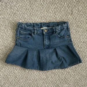 Blå kjol med volang från pomp de lux - Supersöt blå kjol med volang nertill och klassiska fickor fram och bak. Kjolen är gjord i ett stretchigt material som ska efterlikna jeanstyg.  Kjolen har en liten broderad hjärt-detalj på bakfickan. 