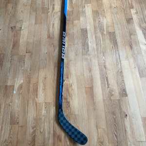 Bauer ZYNC p88 40 Flex  - En modern ishockeyklubba från Bauer Supreme S29-serien. Klubban har en stilren svart design med rutmönster på bladet och blå detaljer på skaftet. Perfekt för unga hockeyspelare som vill ta sitt spel till nästa nivå.