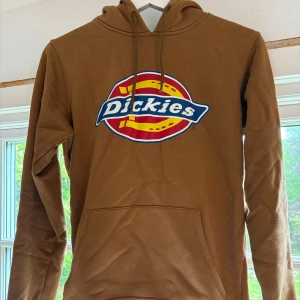Brun hoodie från Dickies - Säljer en brun hoodie från Dickies med stor logga framtill. Tröjan har huva med dragsko och en stor magficka. Perfekt för dig som gillar streetwear och vill ha en bekväm och snygg tröja.