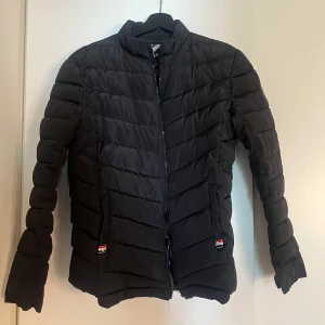 Svart dunjacka från Armani EA7 - Säljer en svart dunjacka från Armani EA7 med diskret glansig finish. Jackan har dragkedja framtill, ståkrage och två fickor med dragkedja. Lätt vadderad och perfekt för kyligare dagar. Klassisk och stilren design med EA7-logga på ärmen. Knappt använd sitter fint och är varm!