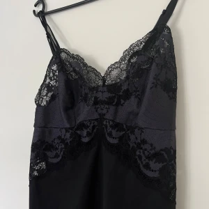Nattlinne, Wacoal, M - Svart satin nattlinne med spetsdetaljer från Wacoal. Storlek M. Klänningen har smala axelband, justerbara. Mycket fin passform och bra kvalite. Nyskick.  65% nylon och 35% spandex/elastan. Spet i 48% polyester (satin), 9% spandex och 43% nylon.   Mått: Längd utan band ca 65 cm Byst ca 38 cm Midja ca 38 cm